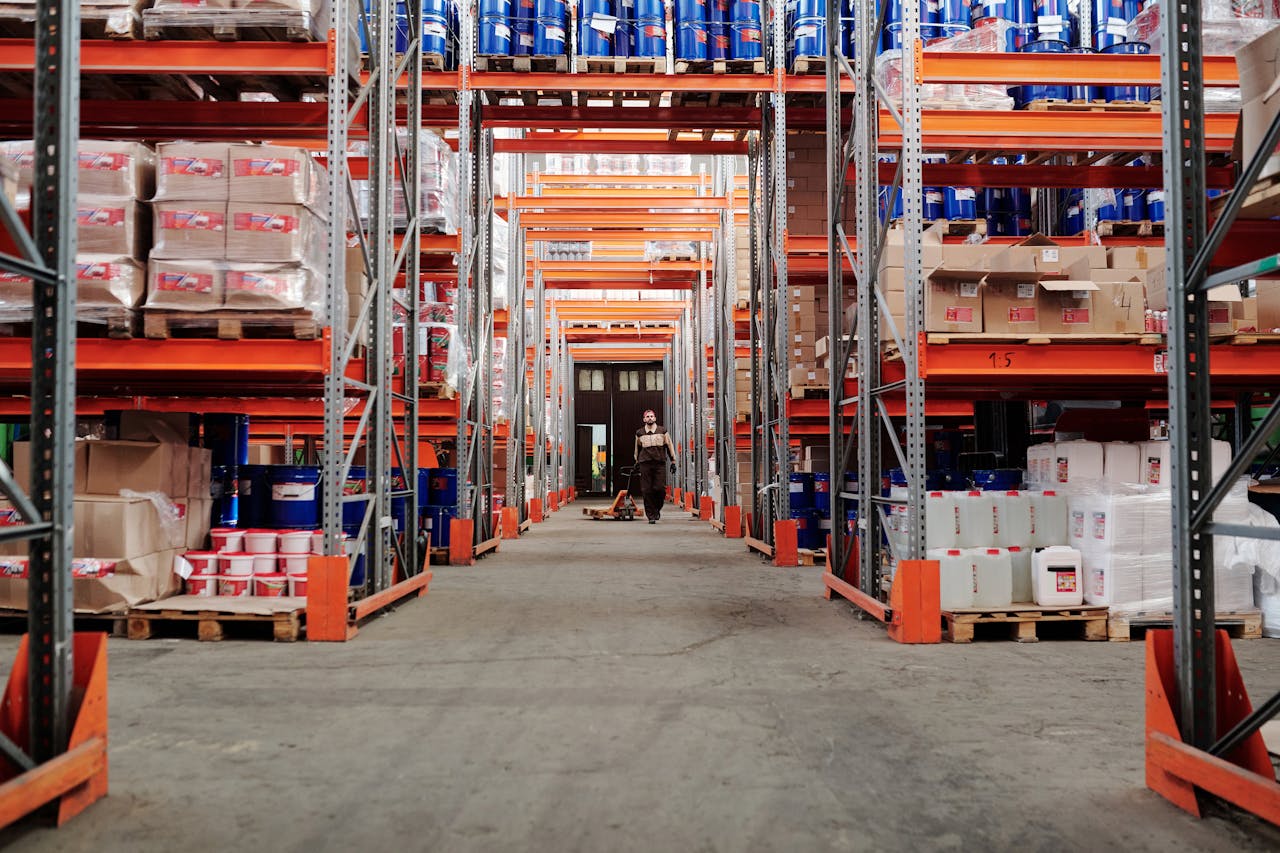 service-01 A spacious industrial warehouse with stocked shelves and a worker in protective gear.