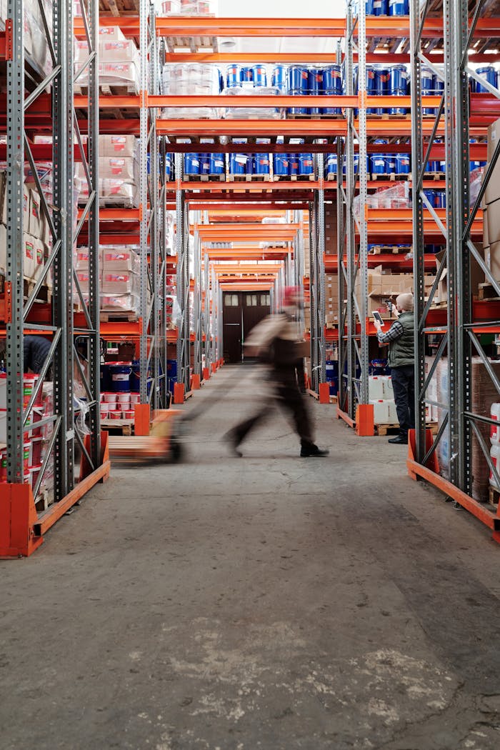 about-01 Blurred motion of a man walking in a spacious warehouse aisle between tall shelves.