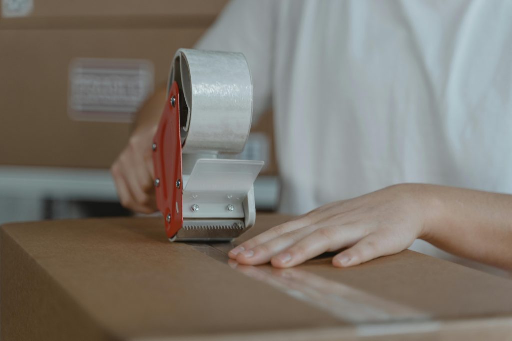 pexels photo 6169036 6169036 A person sealing a cardboard box with tape, emphasizing packaging and shipping processes.
