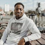 Smiling adult man in a hoodie outdoors, enjoying a sunny day.